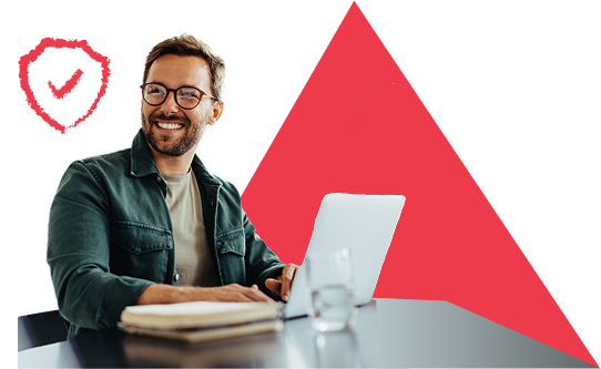 Colleague sitting happily at a desk with a notebook and laptop, smiling, conveying a sense of high performance and psychological safety.